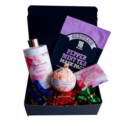 Gift box displaying goodies for the bath - facemask, bubble bath, bath bomb and some sweet treats